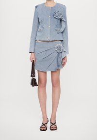 Kurtka jeansowa z złotymi guzikami i kwiatowymi zdobieniami, zestawiona z pasującą mini spódniczką o skręconym designie i ozdobą w postaci róży po bokach.