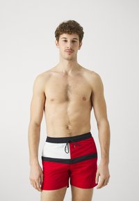Costumi da bagno rossi con dettagli neri e bianchi, dotati di una vita con cordino e di un design sportivo. Tessuto liscio con una texture leggera.