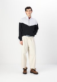 Svart- och vitrandig halvzip-pullover, avslappnade beige byxor och bruna snörstövlar med gummisulor. Har en texturerad tyg och kontrasterande färger.