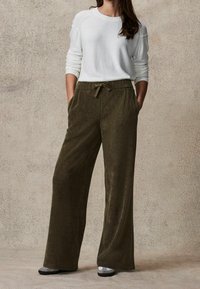 Oliwkowe kordowe spodnie o szerokich nogawkach z przednimi kieszeniami i regulowanym paskiem w talii, połączone z białym swetrem z długim rękawem.