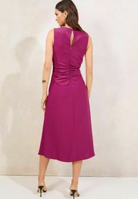 Robe midi en fuchsia avec un corsage ajusté, des détails froncés à l'arrière et une ouverture en forme de clé. Tissu lisse avec un design épuré.