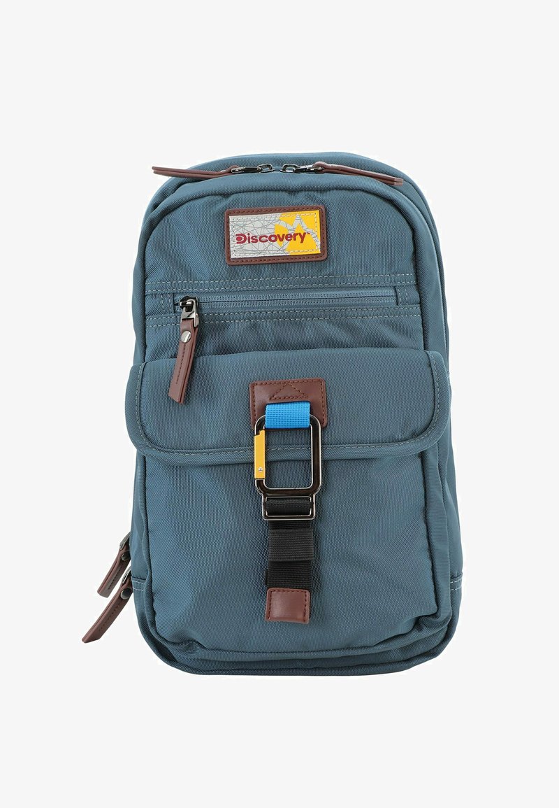 Mochila de tela azul con un acento de cuero marrón, bolsillo frontal con cremallera y una hebilla colorida. Presenta una forma rectangular y una superficie texturizada.