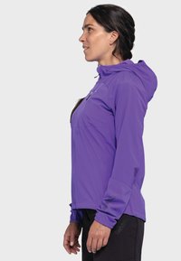Lila Outdoor-Jacke, leichtes Material, Reißverschlussfronttasche, verstellbare Kapuze, elastische Bündchen und Logodetail am Ärmel.