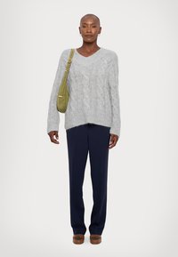 Light gray cable-knit sweater with a V-neck and dropped shoulders, paired with navy blue trousers and a small green handbag. Brown loafers.