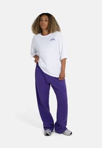 White oversized T-shirt with "ONE EARTH" graphic, paired with loose-fitting purple trousers. Gray sneakers complete the outfit.