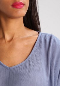 Lyseblå kortærmet top med V-hals, fremstillet i et tekstureret stof med fine plisseringer, der fremhæver en afslappet pasform.