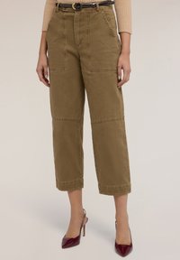 Pantalones cortos de algodón en verde oliva con bolsillos de parche y corte recto. Combinados con tacones de aguja rojos oscuros y un cinturón negro.