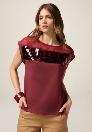 T-shirt bordeaux a maniche corte con scollo trasparente, caratterizzato da un'applicazione di paillettes sul petto. Tessuto di cotone liscio.