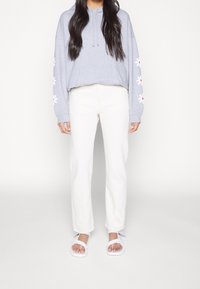 Šedá mikina s květinovými vzory na rukávech, bílé kalhoty s vysokým pasem a rovnými nohavicemi a bílé sandály na pásku. Jednoduchý, pohodlný outfit.