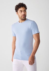Tricou scurt cu mâneci scurte de culoare albastru deschis, fabricat dintr-un material moale. Design ajustat cu decolteu rotund și textură netedă. Purtați cu pantaloni albi.