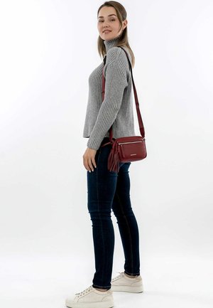 Bolso cruzado de cuero rojo con superficie texturizada, correa ajustable y bolsillo frontal con cremallera. Presenta un borlas decorativa en el lateral.