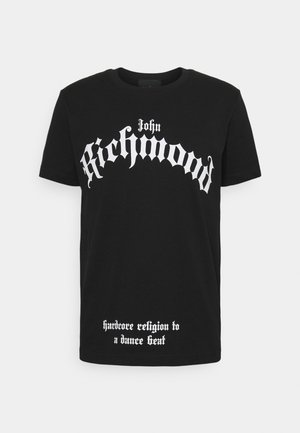Musta T-paita, jossa rinnassa suuri valkoinen goottilainen teksti "John Richmond" ja helman lähellä pienemmällä tekstillä "hardcore religion to a dance beat".