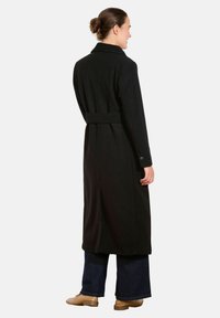 Długi czarny płaszcz z paskiem w talii, z wyciętym kołnierzem i zapięciem na guziki przy mankietach. Wykonany z mieszanki wełny, o prostym kroju i z bocznymi rozcięciami.