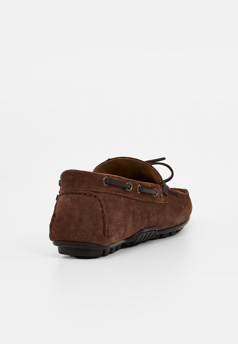 Braune Wildleder-Mokassinschuhe mit abgerundetem Zehenbereich, dekorativer Schnürung und schwarzer Gummisohle. Strukturiertes Obermaterial mit Nähdetails.