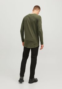 Olivgrünes Langarmshirt mit abgerundetem Saum, kombiniert mit schwarzen Slim-Fit-Hosen und schwarzen Stiefeln, von hinten betrachtet.