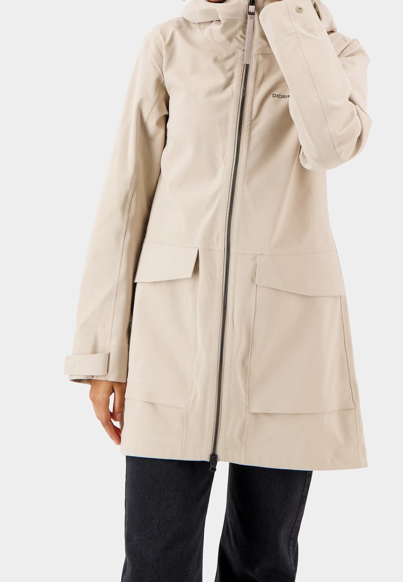 Světle béžová nepromokavá bunda s plným předním zipem, nastavitelnou kapucí a dvěma velkými předními kapsami. Vyrobena z hladké, texturované látky.