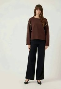 Pull marron à manches larges avec des coutures blanches le long des bords, associé à un pantalon large noir. Design simple et épuré.
