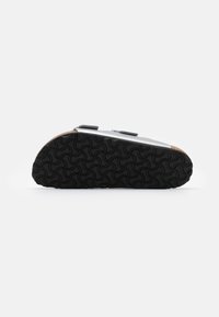 Svart gummisåle med bølgete mønster, grått overmateriale, to justerbare stropper, rund form og korkdetaljer langs bunnen.