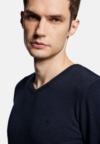 Granatowy sweter w serek wykonany z miękkiej dzianiny, z subtelnym logo na klatce piersiowej i teksturowanym dekoltem.