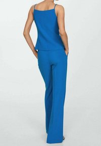 Niebieski top bez rękawów z dopasowanym dołem w kształcie litery A, zestawiony z niebieskimi spodniami o szerokich nogawkach. Gładka tkanina w jednolitym kolorze, bez widocznych wzorów.