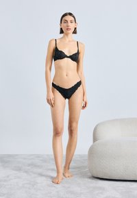 Ensemble soutien-gorge et culotte en dentelle noire avec bords festonnés. Le soutien-gorge est doté de bretelles réglables ; la culotte a une coupe taille basse.