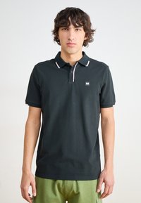 Sort polo t-shirt med korte ærmer, pink trim ved krave og manchetter, med et lille logo patch på brystet. Materialet er bomuld.