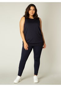 Navy mouwloos top met een relaxte pasvorm, gecombineerd met bijpassende leggings. Gladde, rekbare stof zonder zichtbare patronen of accenten. Witte sneakers.