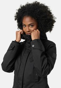 Black waterproof jacket with a high collar, adjustable cuffs, and logo patch. Features a smooth texture and button details.