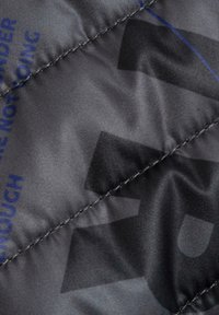 Gråt quiltet stof med en glat tekstur, med blå trykt tekst og et sort geometrisk mønster, syet med en kontrastfarvet tråd.