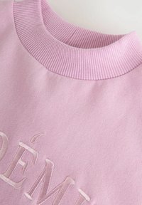 Jasnoróżowy sweter z teksturowanym prążkowanym kołnierzem i haftowanymi detalami. Miękka tkanina, średnia waga i luźny krój.