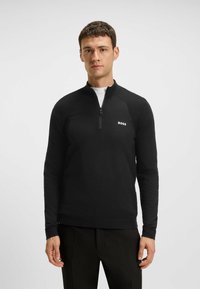 Schwarzer Zip-Hals-Pullover mit gerippter Textur an den Schultern und einem kleinen weißen "BOSS"-Logo auf der linken Brust. Lange Ärmel, taillierte Passform.