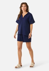 Ensemble deux pièces bleu marine comprenant un haut à col et manches courtes ainsi que des shorts assortis. Texture tissée, coupe décontractée et tissu léger.