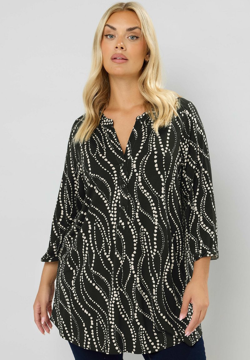 Svart tunika blus med knäppning fram, prydd med vita vågiga linjer och prickmönster, 3/4 ärmar och avslappnad passform.