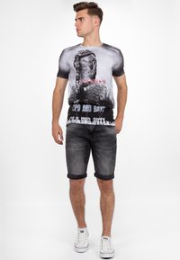 Grafische T-shirt met een zwart-wit ontwerp van een gezicht, gecombineerd met grijs denim shorts met omgeslagen zoom en witte sneakers.