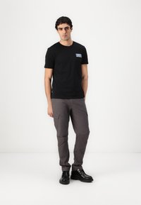 Sort bomulds t-shirt med en blå label, parret med grå cargo bukser med sidelommer og tapered ben. Fodtøj: sorte sko.