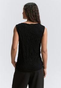Schwarzes ärmelloses Oberteil aus strukturiertem, zerknittertem Stoff. Lockerer Schnitt und runder Halsausschnitt, mit rohen Kanten und minimalistischem Design.