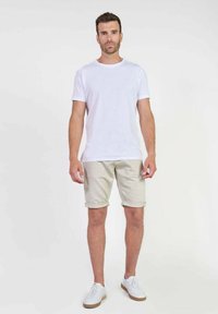 T-shirt en coton blanc, shorts beiges clairs et baskets blanches. Look décontracté avec un design simple, sans motifs ni logos visibles.