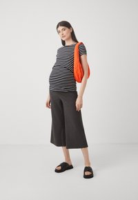 Pruhované čierno-biele tehotenské tričko, v kombinácii so šedými rebrovanými culottes. Modelka má v ruke oranžovú prešívanú tašku a na nohách čierne sandále.