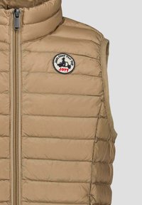 Beige gewatteerd vest met een hoge kraag, ritssluiting en armsgaten. Voorzien van een rond logo met de tekst "Just Over the Top JOTT." Gladde textuur.