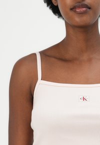 Light pink ribbed tank top with thin straps and a square neckline, featuring a small Calvin Klein logo patch at the center.
