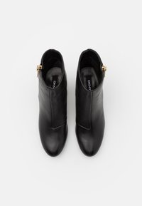Botines de cuero negro con un diseño elegante, que cuentan con una cremallera dorada lateral y un puntero afilado. Textura suave, estilo minimalista.