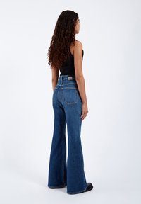 High-waisted flared jeans in medium blue denim, featuring two back pockets and a stitched logo above the waistband.
