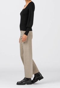 Haut noir à manches longues avec un col carré, accompagné d'un pantalon beige large aux bords effilochés et de bottines noires épaisses.