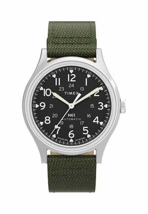 Timex MK1 automata óra fekete számlappal, fehér számokkal, fluoreszkáló mutatókkal, ezüst tokban és texturált sötétzöld szövet szíjjal.
