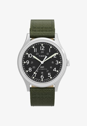 Timex MK1 Automatik-Uhr mit schwarzem Zifferblatt, weißen Ziffern, leuchtenden Zeigern, silbernem Gehäuse und strukturiertem dunkelgrünem Stoffarmband.