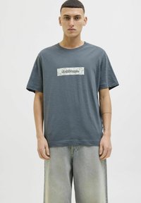 Pilkas medvilninis marškinėliai trumpomis rankovėmis, su stačiakampiu, raštuotu įsiuvu, viduryje turi "Jack & Jones" logotipą. Atsipalaidavęs fasonas.