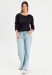 Black, textured long-sleeve sweater paired with light blue, high-waisted wide-leg jeans and white sneakers with brown accents.