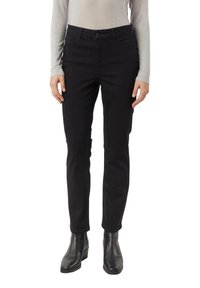 Žena v úzkých černých kalhotách, černých kotníkových botách a světle šedém topu s dlouhým rukávem, stojící s uvolněnýma rukama po stranách.