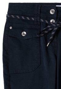 Pantalon bleu marine foncé avec poche avant à rabat fermée par un bouton en métal et cordon de serrage bleu marine à motifs noué à la taille.