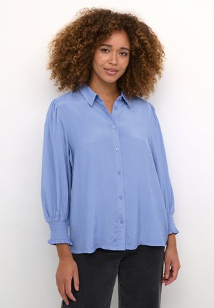 Light blue button-up shirt with a collar, puff sleeves, and smocked cuffs. Made from smooth fabric with a relaxed fit and curved hem.
